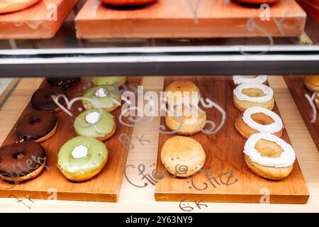 Donuts mit verschiedenen Geschmacksrichtungen und Belägen werden an einem lokalen Imbissstand ausgestellt Stockfoto