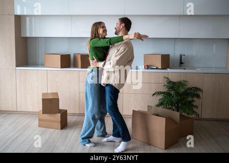 Glückliche, überglückte Frau und Mann umarmten sich in der Küche und zogen in eine neue Wohnung zwischen Pappkartons Stockfoto
