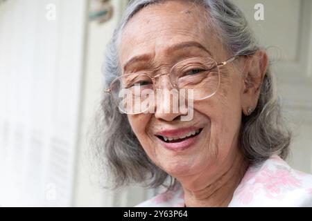 Gesunde südostasiatische ältere Frau in Brille lächelnd und in die Kamera schauend Stockfoto
