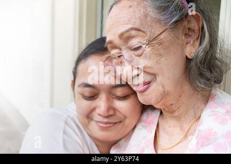 Eine glückliche Erwachsene Tochter aus Asien, die ihre alte Mutter umarmt, wenn sie zu Hause ist Stockfoto