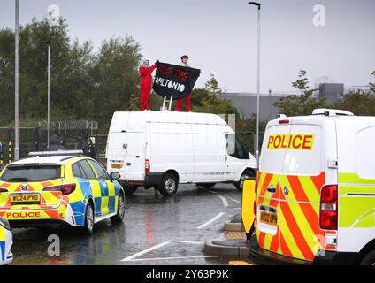 Polizeifahrzeuge umzingeln den Van, während die Demonstranten während einer Demonstration ein Banner darauf schwenken. Palästinensische Aktivisten blockieren die Zufahrtsstraße im Forschungszentrum des israelischen Waffenherstellers Elbit Systems in Filton, Bristol, produziert Elbit Drohnen, die derzeit gegen Palästinenser in Gaza und anderswo eingesetzt werden. Die Demonstranten wollten auch den Fall der Filton10 hervorheben, die alle verhaftet wurden, als propalästinensische Aktivisten im August 2024 in die Fabrik von Elbit Systems eindrangen. Sie wurden aufgrund eines Antiterrorgesetzes verhaftet, das der Polizei die Möglichkeit gibt, zu beschaffen Stockfoto