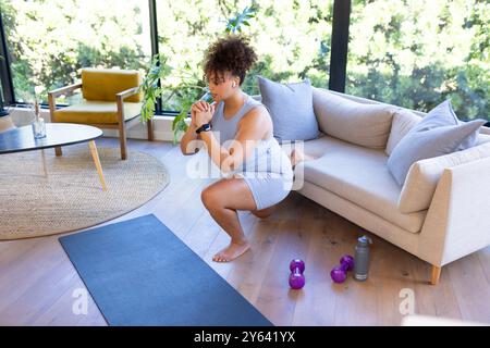 Sport zu Hause, Frau, die Squats auf Yogamatte macht, mit Kurzhanteln in der Nähe, zu Hause, zu Hause Stockfoto