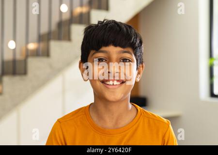 Lächelnder Indianer in orangefarbenem Hemd, der drinnen steht und in die Kamera schaut Stockfoto