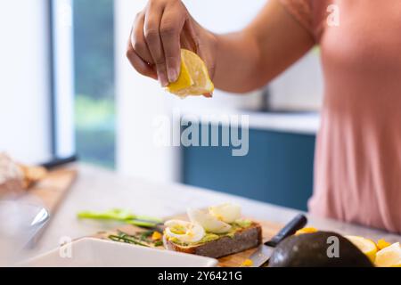 Zitrone auf Avocadotoast drücken, Frau bereitet gesundes Frühstück in der Küche, zu Hause, zu Hause Stockfoto