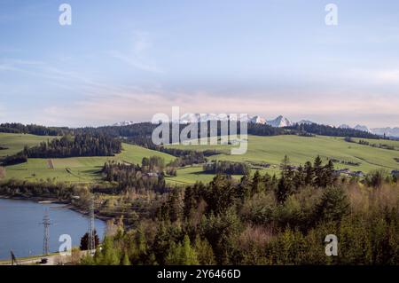 Blick auf die schneebedeckten Gipfel der Tatra und Wiesen, Wald, grüne Hügel an einem sonnigen Tag vom Damm am Czorsztyn-See. Panorama der Tatra Stockfoto