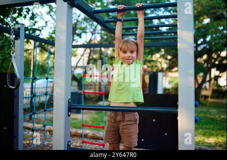 Ein Kind klettert an einem sonnigen Nachmittag souverän auf Spielgeräten unter klarem Himmel, umgeben von Grün Stockfoto