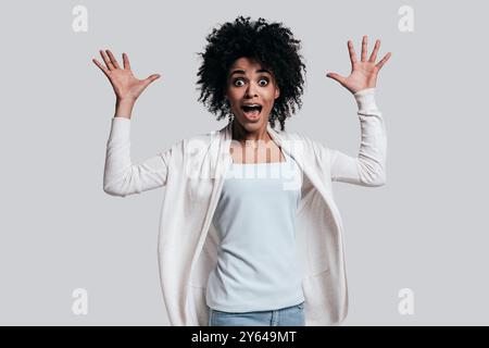 Total schockiert. Überraschte junge Afrikanerin mit geöffnetem Mund und Blick auf die Kamera, während sie vor grauem Hintergrund stand Stockfoto