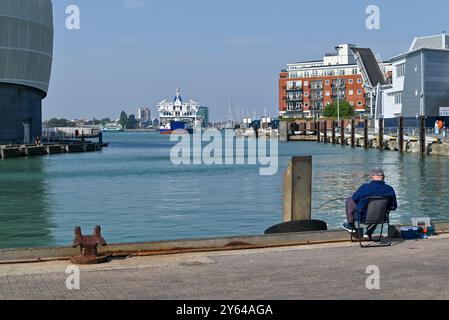 Mann, der sich entspannt und angelt am Camber Dock mit einer Fähre auf der Isle of Wight in der Ferne. September 2024. Stockfoto