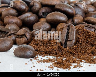 Makrofoto von Kaffeebohnen und einem kleinen Stapel frisch gemahlenen Kaffees auf einer Keramikoberfläche. Stockfoto