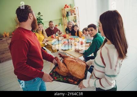 Foto von fröhlichen jungen Leuten, Ehepartner halten Tisch gefüllt gebackenes leckeres traditionelles Fleisch truthahn Thanksgiving Tag drinnen Stockfoto