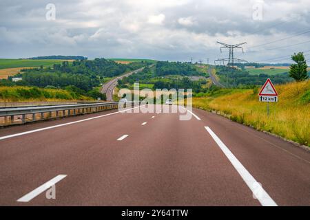 Frankreich, zweispurige Autobahn schlängelt sich durch die Landschaft mit grünen Feldern und bewölktem Himmel Stockfoto