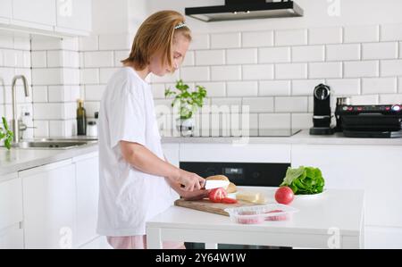 Das kleine Mädchen schneidet Eine Tomate auf dem Brett mit Einem Messer in der Küche Stockfoto