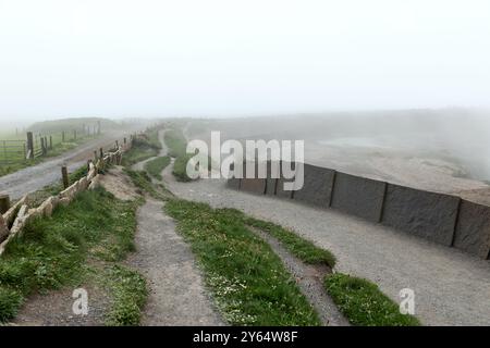 Ein nebeliger Wanderweg entlang der Cliffs of Moher im County Clare, Irland, bietet zerklüftetes Gelände und Granitzäune. Dichter Nebel umhüllt die Kap Stockfoto