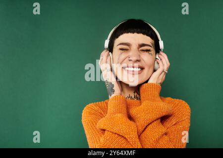 Eine junge Frau mit kurzen Haaren und Tätowierungen lächelt hell, während sie einen gemütlichen Pullover in einem warmen Studio trägt. Stockfoto