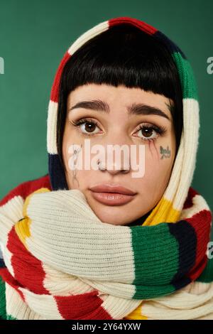 Eine junge Frau mit kurzen Haaren und Tätowierungen umarmt einen warmen Pullover und Schal in einem Studio. Stockfoto