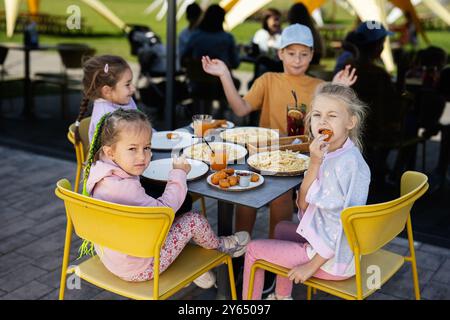 Vier Kinder sitzen an einem Tisch und genießen Snacks und Getränke in einem Café im Freien. Die Szene fängt Glück, Freundschaft und einen gemütlichen Moment in einem ein Stockfoto