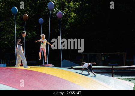 Kinder genießen eine Outdoor-Aktivität auf einer großen, farbenfrohen, hüpfenden Fläche auf einem Spielplatz. Eine lebendige Szene mit lebhaften Ballons im Hintergrund unter cl Stockfoto