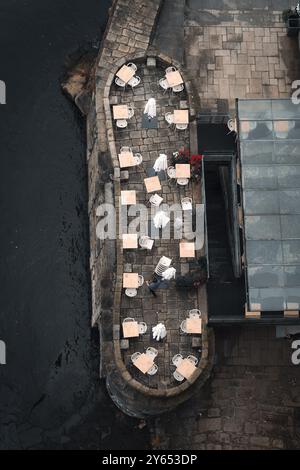 Blick aus der Vogelperspektive auf ein Café im Freien mit leeren Tischen und Stühlen auf einer Steinterrasse am Wasser. Stockfoto