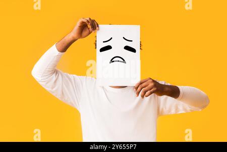 Schwarzer Mann, Papier mit traurigen Emoji über sein Gesicht Stockfoto