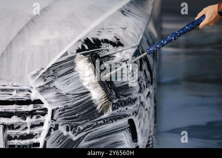 Man wäscht ein Auto mit einer speziellen Bürste in einer Autowaschanlage. Nahaufnahme von man Wash linker Scheinwerfer. Das Auto ist in Schaum Stockfoto