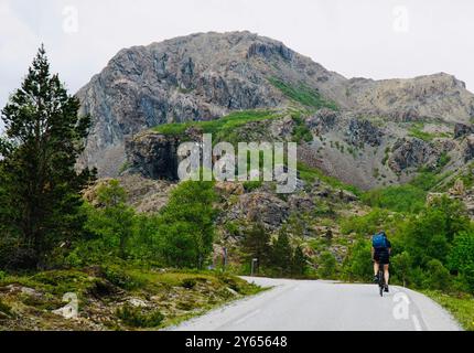 Ein Mann, der auf einer malerischen Straße auf der Insel Leka, Norwegen, mit Felsformationen und üppigem Grün im Hintergrund radelt Stockfoto