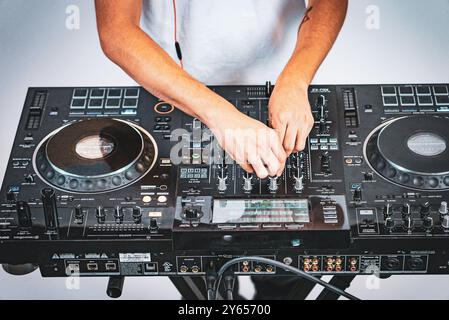 Nahaufnahme eines DJ, der Musik auf einem professionellen DJ-Controller mischt, wobei die Hände die Bedienelemente und Details der Ausrüstung anpassen. Stockfoto