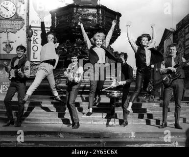 Liverpool - Gruppe " The Swinging Blue Jeans " auf den Stufen von Eros im Piccadilly Circus mit Models im " Swinging Blue Jeans " Look . Die Firma Lybro Ltd hat eine " Uniform " für die Mädchen im Teenageralter entworfen , die sich wie ihre Pop-Idole kleiden wollen . Das Outfit besteht aus einer Jeans , einem Jeanjak , einer kurzen Jacke ohne Kragen und einem Hemd mit Kragen . Die Modeschau hält sich an den Mersey Beat , alle Modelle (von links nach rechts) : Pat Robinson , Cherry Goff und Edwina Spencer , alle aus Liverpool . November 1963 Stockfoto