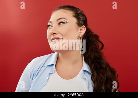 Eine atemberaubende Frau in Übergröße zeigt leuchtendes Make-up und Selbstvertrauen, während sie vor einem leuchtend roten Hintergrund posiert. Stockfoto