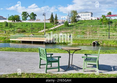 Jelabuga, Russland - 22. Mai 2024: Runder Tisch und zwei Holzstühle auf dem Weg in der Nähe des Teichs. Ein Ort zur Erholung im Kultur- und Erholungspark Shishkin Ponds. Stockfoto