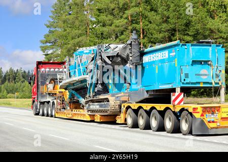 Roter Scania 730S Lkw, der Powerscreen Chieftain 2100X geneigte Scheibe auf Tieflader-Anhänger entlang der Straße transportiert. Jokioinen, Finnland. August 2024. Stockfoto