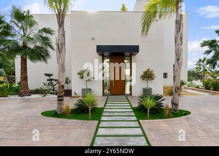 Ein moderner Villeneingang mit einem symmetrischen Gartenweg, umgeben von üppigen Palmen und dekorativen Pflanzen, bietet einen Luxus und in sich Stockfoto