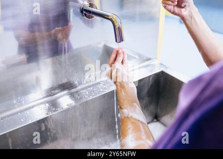 Ein medizinisches Fachpersonal wird in einem chirurgischen Spülbecken mit Seife und Wasser sorgfältig ihre Arme und Hände reinigen und dabei ein ordnungsgemäßes Hygieneprotokoll demonstrieren Stockfoto