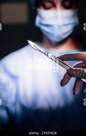 Ein Nahbild zeigt einen Chirurgen, der eine blaue chirurgische Maske trägt. In der Nähe hält ein anderer Arzt ein Skalpell klar im Fokus, das Fokus A darstellt Stockfoto