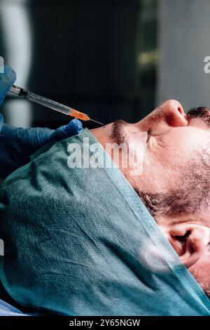 Eine detaillierte Ansicht eines männlichen Patienten, der in einem Operationsraum eine Narkoseinjektion erhält, mit blauen Handschuhen der Hände eines Arztes Stockfoto