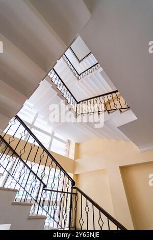 Ein fesselnder Blick vom Boden einer mehrstöckigen Wendeltreppe mit kunstvollen Eisenbalustraden und hellen Innenräumen Stockfoto