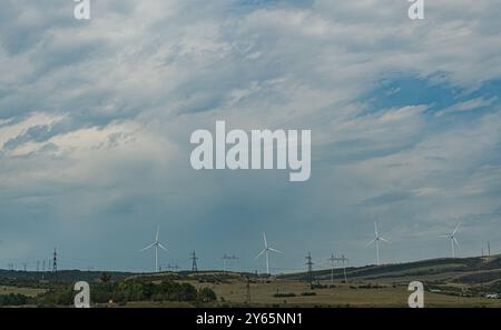 Dieses Bild zeigt die ruhige ländliche Landschaft Georgiens mit sanften Hügeln und modernen Windturbinen vor dem Hintergrund eines dynamischen bewölkten Himmels Stockfoto