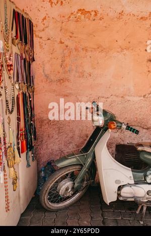 Ein Vintage-Motorrad, das vor einer strukturierten, abblätternden Wand geparkt ist und mit einer Vielzahl von bunten Accessoires und Kunsthandwerk in Marrakesch geschmückt ist Stockfoto