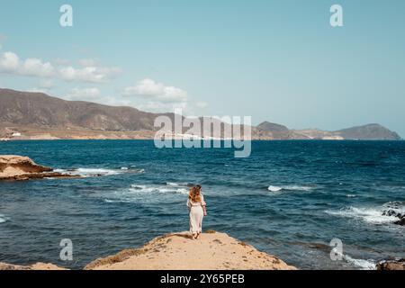 Rückansicht einer nicht erkennbaren Frau, die ein weißes Kleid trägt, mit Blick auf das Mittelmeer am Strand, Cabo de Gata, Almeria, Spanien. Stockfoto