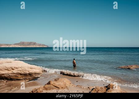 Rückansicht eines nicht erkennbaren Mannes, der in den ruhigen Gewässern von Cala Plomo, Cabo de Gata, Almeria, Spanien steht, mit beeindruckenden Küstenklippen in der Stockfoto