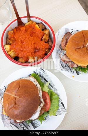 Zwei köstliche Burger mit frischem Salat und Tomaten zusammen mit einem Teller Pommes frites in Tomatensauce serviert auf einem weißen Tisch Stockfoto