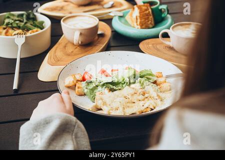 Geerntete, nicht erkennbare, anonyme, gesichtslose Person, die auf Caesar Salat mit gegrilltem Huhn, Croutons und Kirschtomaten gegessen hat, begleitet von einer Variette Stockfoto