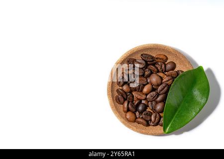Geröstete Kaffeebohnen in einer kleinen Holzschale neben einem leuchtenden grünen Blatt auf weißem Hintergrund, perfekt für Themen im Zusammenhang mit Coffee sc Stockfoto
