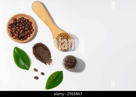 Kaffeebohnen, eine Bürste und ein Kaffeespeeling in einer Holzschale und einem Glas, die neben grünen Blättern für ein frisches, biologisches Gefühl präsentiert werden, ideal für Körperpflegeroutinen Stockfoto