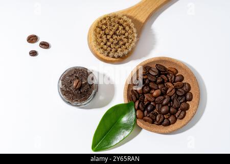 Ein ordentlich angeordnetes Kaffeespeeling in einem Glas, mit ganzen Bohnen in einer Holzschale und einer natürlichen Bürste auf weißem Hintergrund, die Bio-Skinca symbolisiert Stockfoto