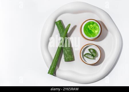 Aloe Vera-Blätter und natürliches grünes Gel in zwei kleinen Holztöpfen, die auf einem eleganten weißen Tablett platziert werden, betonen die Verwendung von Aloe-Gel sowohl im Gesicht als auch im Körper c Stockfoto