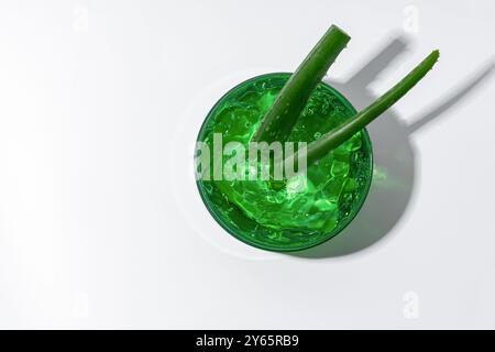 Hellgrünes Aloe Vera-Gel in einem transparenten Glas mit frischen Aloe Vera-Blättern, die im Inneren deutlich sichtbar sind, beleuchtet durch sanftes, natürliches Licht Stockfoto
