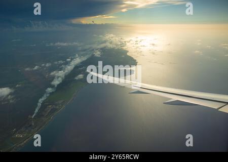 Die ruhige Luftperspektive aus einem Flugzeugfenster fängt den Sonnenuntergang über einer ruhigen Küstenlandschaft und glitzerndem Wasser ein. Stockfoto