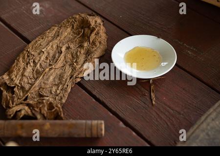 Eine Nahaufnahme der wichtigsten Elemente, die in der traditionellen kubanischen Zigarrenherstellung in Vinales verwendet werden, mit getrockneten Tabakblättern und einer Schüssel Honig Stockfoto