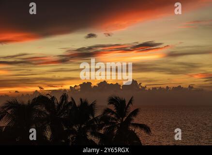 Ein atemberaubender Sonnenuntergang mit leuchtenden orange und roten Wolken über dem Meer, eingerahmt von Silhouetten Palmen in Varadero, Kuba, dem ruhigen und malerischen s Stockfoto