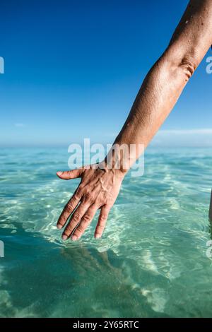 Zugeschnittener, nicht erkennbarer Blick auf die Hand einer Frau, die sanft das ruhige Wasser des Karibischen Meeres in Varadero, Kuba, berührt und eine friedliche Interaktion zeigt Stockfoto